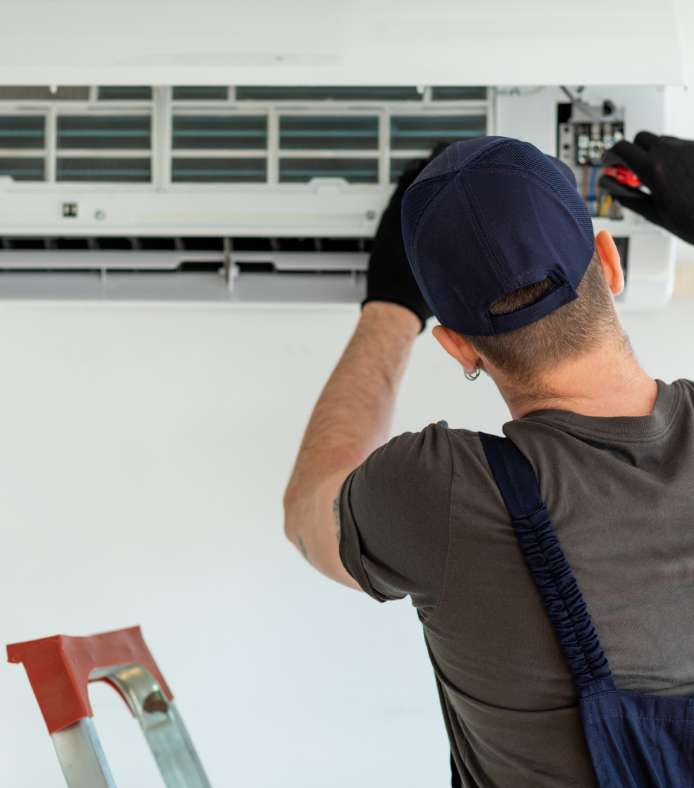 A man providing HVAC services facing away from the camera to install or repair a wall mounted heat pump